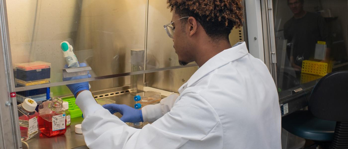 A student in a white lab coat using lab equipment